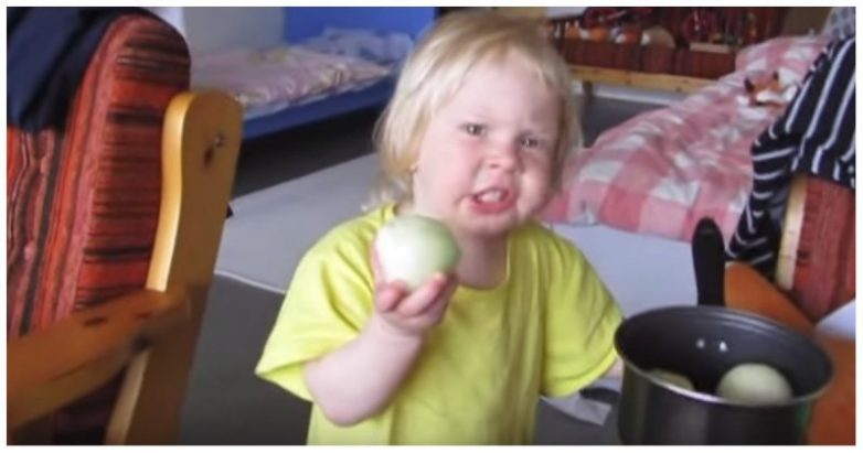 Настырная девочка пытается есть лук как яблоко