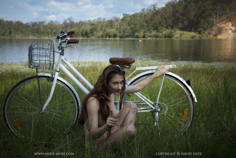 Обнаженная красотка на велосипеде у реки